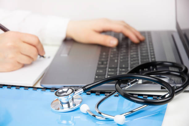 Doctor working in modern medical office, making notes and using laptop. Medical education and online medicine concept