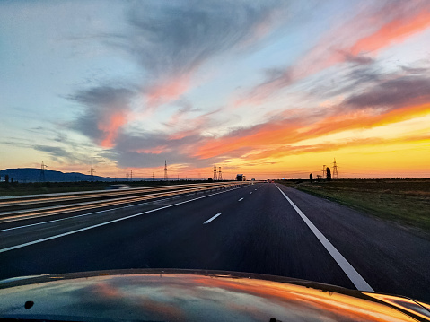 The view from the car's windshield to the beautiful sunset, a large highway. Traveling by car. Beautiful orange sky at sunset. Horizontal photo.