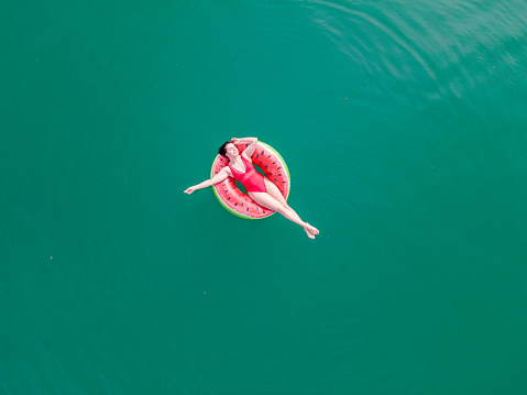 young happy woman floating in blue azure water on inflatable ring circle summer vacation