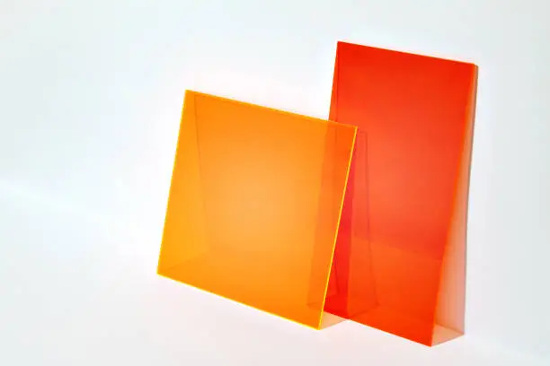 Red and orange acrylic shapes on a bright lit white background. Colourful minimalist stage for advertising, promoting, exhibition new products. Stylish abstract backdrop with space for text.