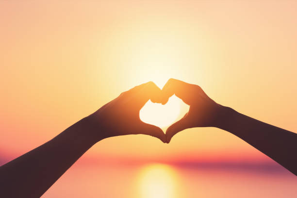 istock Female hands heart shape on sunset sky at tropical beach abstract background. 1364213904