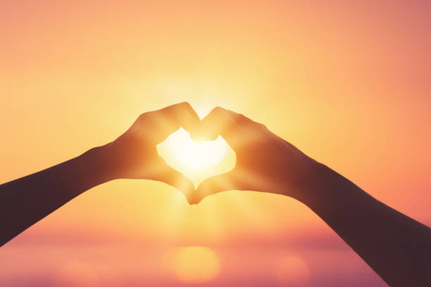istock Female hands heart shape on sunset sky at tropical beach abstract background. 1364213927