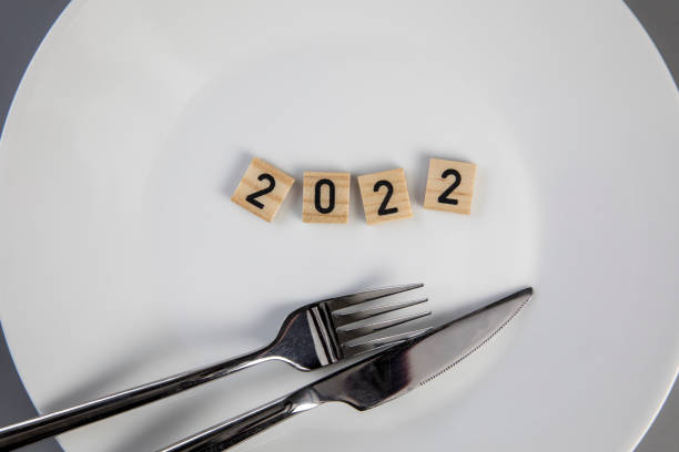 istock Fork and knife on a white empty plate with 2022 text top view, New year diet, healthy eating concept background 1364216475