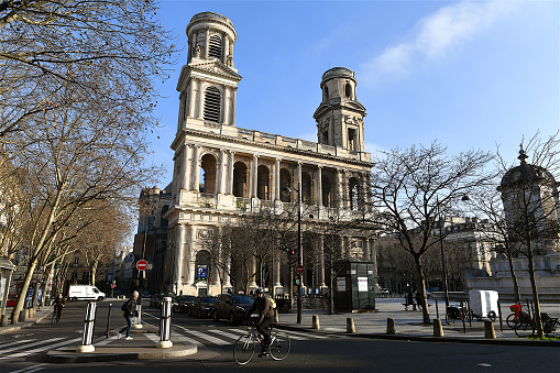 Cyclist and pedestrians passing in front of the Saint-sulpice church. Saint-Sulpice is a Roman Catholic church in Paris, France, in the Odéon Quarter of the 6th arrondissement. It is the second largest church in the city after Notre Dame Cathedral.