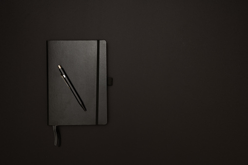 Top view of black photorealistic notebook on black background.