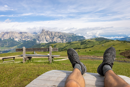 The legs of a hiker lying on a bench surrounded by a scenic landscape. Shot in South Tyrol, Italy.