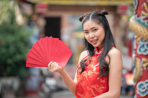 Beautiful portrait young Asian woman cheongsam dress smiling holding red envelope, girl celebrate with exciting, happy Chinese New Year, holiday concept.