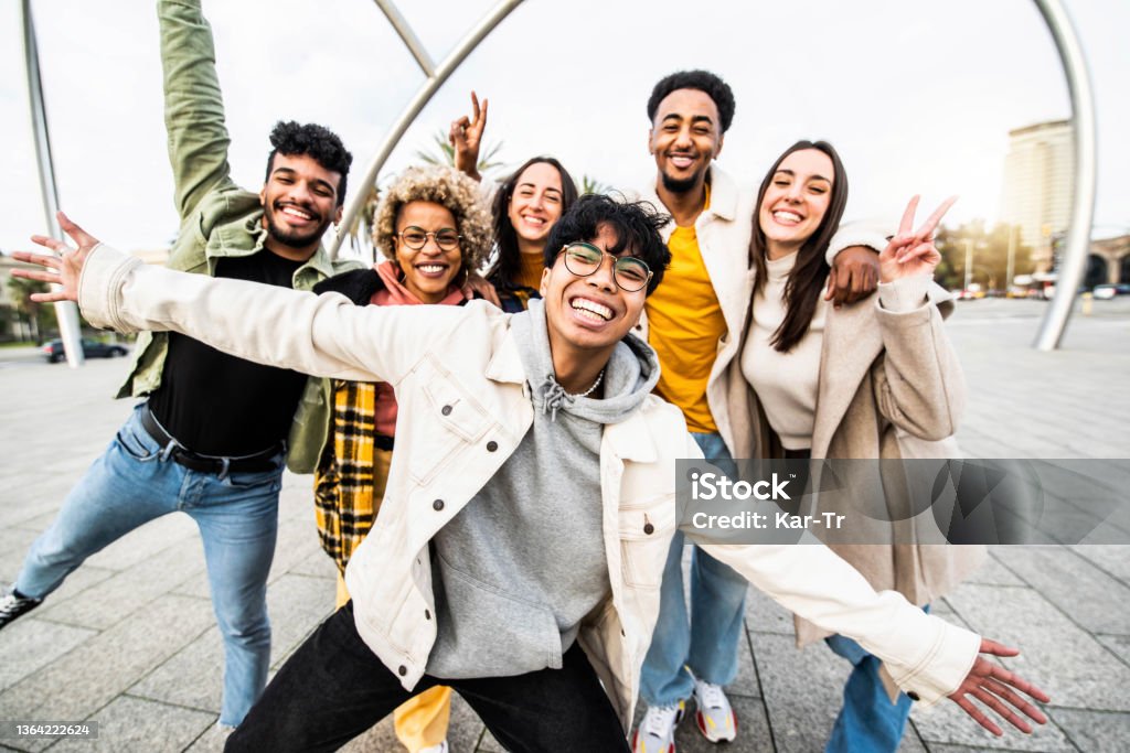Big group of happy friends stands together on city street with raised arms - Multiracial young people having fun outside - Volunteer with hands up showing teamwork spirit - Community and friendship University Student Stock Photo