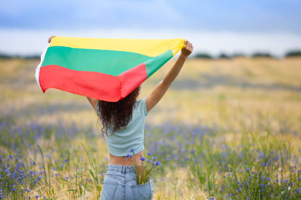 Young woman holding flag of Lithuania in a rye field with blue cornflowers. stock photo