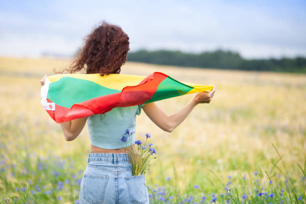 Woman holding flag of Lithuania in a rye field with blue cornflowers. stock photo