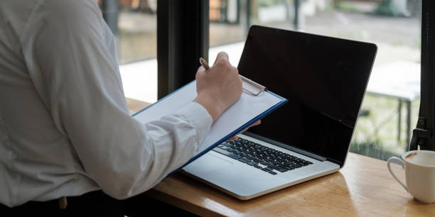 istock Business woman hand are taking notes on paper with a pen, and she is using a laptop computer on a wooden desk in the office.Web banner 1364223709
