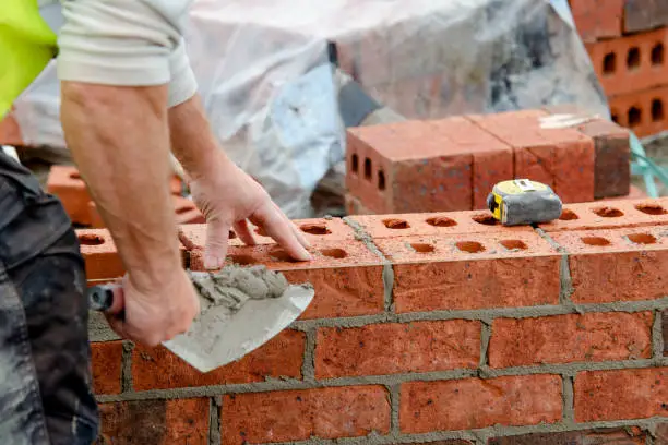 Bricklayer laying bricks on mortar on new residential house construction