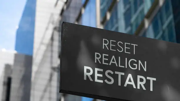 Reset Realign Restart on a black city-center sign in front of a modern office building