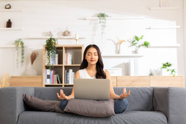 Clam of Asian young woman doing yoga lotus pose to meditation and relax on couch during work online at home.Happiness female break after worked close her eyes and deep breath with yoga so peaceful. almeja de mujer joven asiática haciendo postura de loto de yoga para meditar y relajarse en el sofá durante el trabajo en línea en casa. felicidad femenina descanso después de trabajar cerrar los ojos y respirar profundamente con yoga tan tranquilo.