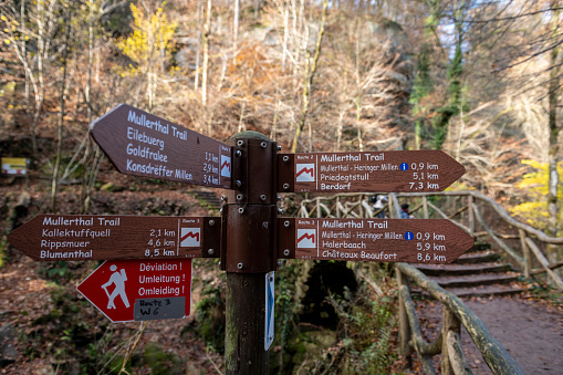 Direction and distance signs point the way to various destinations for people hiking near the Schiessentümpel waterfall in Luxembourg.