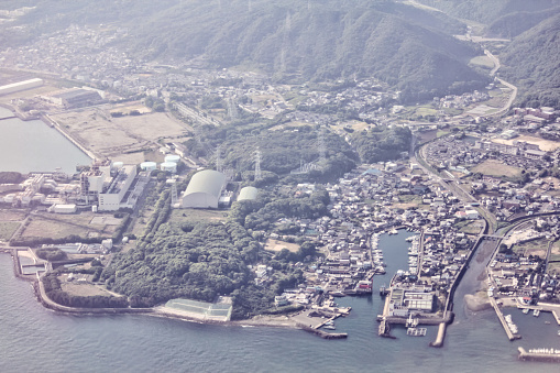 A seaside town in Japan seen from a bird's eye view from a plane overlooking the sea, ports, industrial plants and transport.