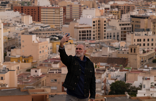 Portrait of adult man taking picture of himself with cellphone against city, Almeria, Andalusia, Spain