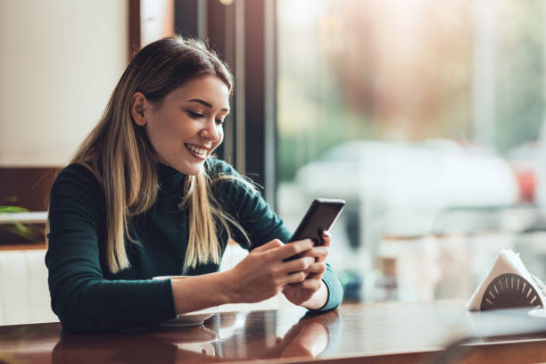 istock Young happy woman at restaurant drinking coffee and using mobile phone. 1364246400