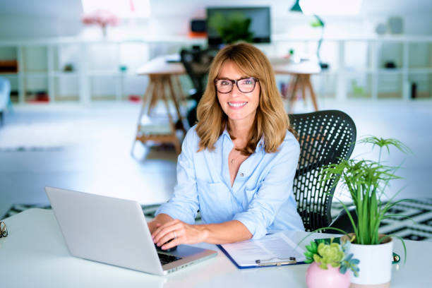 istock Middle aged businesswoman using laptop while sitting at office desk and working 1364246442