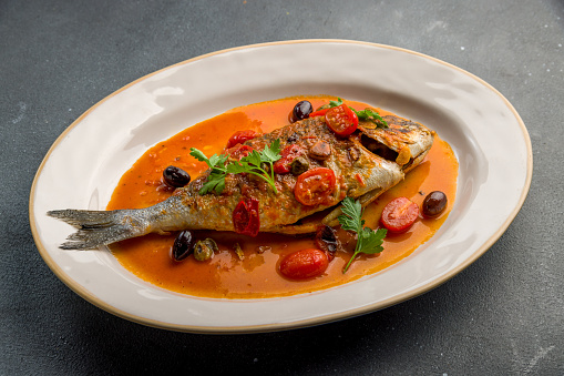 Dorado on grill in tomato sauce on a white plate on grey concrete table