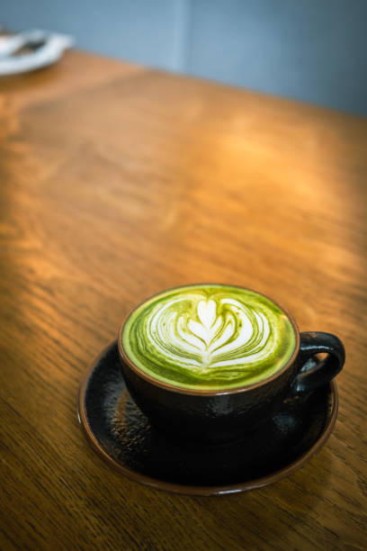 Image of a hot matcha green tea latte coffee with latte art on wooden table.