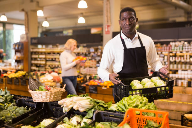 istock Salesman putting vegetables on store showcase 1364255353