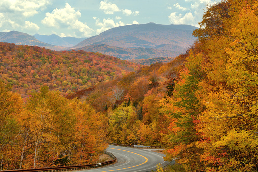 Scenic vista from roadside near top of Kinsman Notch Mountain pass in New Hampshire. Breathtaking view of vibrant fall foliage and tall peaks of mountains in White Mountain National Forest.