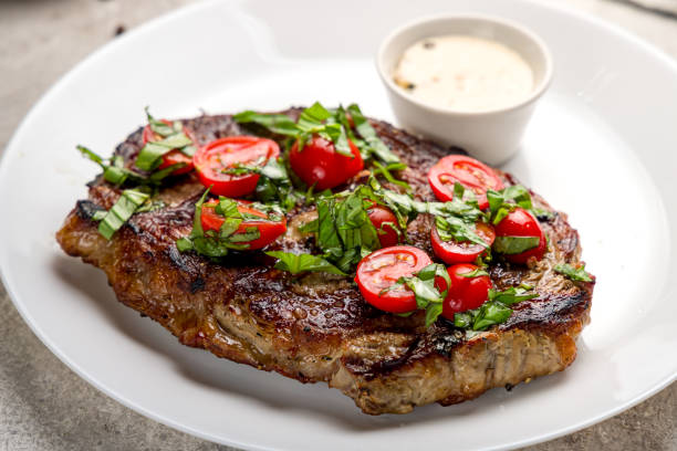 istock juicy Ribeye steak with fresh tomatoes on white plate on grey concrete table macro close up 1364261070