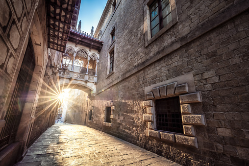 Sun below the Bishop Bridge at the empty medieval alley in gothic quarter, Barcelona, Spain