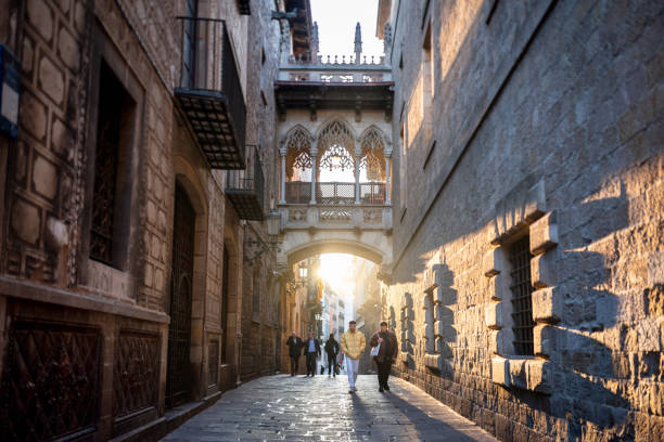 December 14, 2021 - Barcelona, Spain:  Group of people walking early in the morning in the narrow streets of the Gothic Quarter in Barcelona, below the Bishop Bridge
