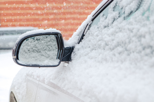 Frozen rearview mirror, snowy car. Winter snow snowfall.