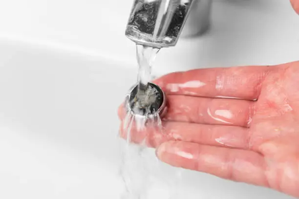 Photo of Washing the clogged filter aerator of a bathroom faucet sink with calcium sediments on the plumbers hand under running water. Plumbing repair