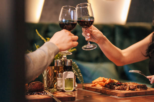 Close up shot of man and woman toasting and drinking red wine from glasses on dinner