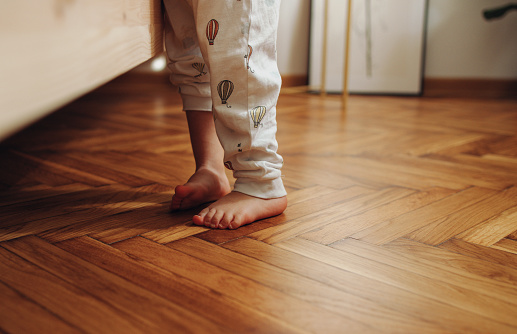 Cropped photo of a child's legs in pyjamas standing barefoot on the wooden herringbone flooring.