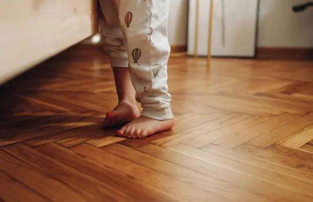 Cropped photo of a child's legs in pyjamas standing barefoot on the wooden herringbone flooring.