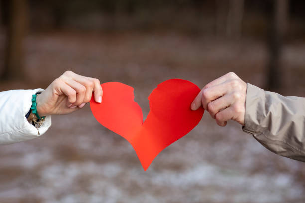 dos manos, macho y hembra, lágrima de corazón rojo símbolo de los amantes contra el fondo del bosque de invierno. oncepto de romper relación. el amor ha terminado. resentimiento y separación. - separación fotografías e imágenes de stock