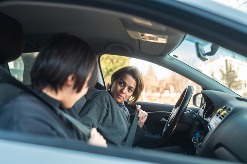 A female driving school instructor is teaching how to drive to a young woman.