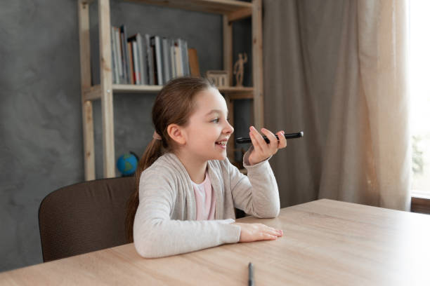 assistente vocale. la ragazza felice detta il testo usando il microfono dello smartphone o del telefono cellulare. studente al telefono registra un messaggio audio. registrazione vocale sms. - one kid only audio foto e immagini stock