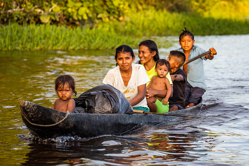 Orinoco, Venezuela - 11-23-2021: Family of native indigenous Orinoco tribe swimming in traditional wooden canoe on the river