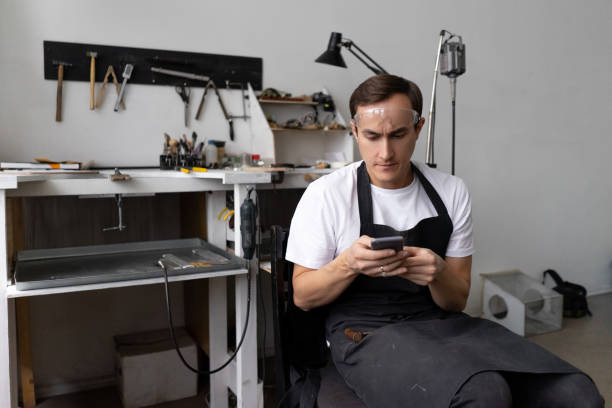 istock Male worker in a workshop sits in a smartphone screen. Leisure during work break. 1364304336