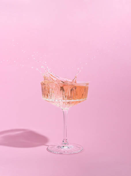 スプラッシュとガラスのピンクのシャンパン。ピンクの背景。クリエイティブな最小限のコンセプト。 - クリスタルガラス ストックフォトと画像