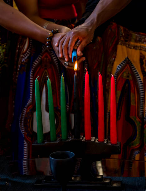 kwanzaa-feier, nahaufnahme der familie, die die kinara-kerze im geiste der einheit anzündet - kinara stock-fotos und bilder