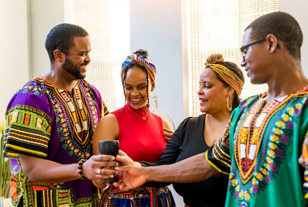 Kwanzaa celebration, African American family holding the unity cup together at home with kinara Kwanzaa celebration black culture photos stock pictures, royalty-free photos & images