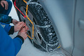 Adult man showing adult woman how to put on car tire chains.