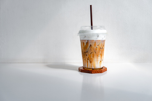 Iced caramel macchiato coffee in a plastic cup on a wooden table at the cafe. Cold espresso in the coffee shop with copy space. Beverage glass frozen in the restaurant. Food sales busy interior decoration vintage.