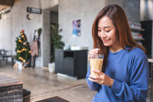 Portrait image of a young asian woman holding and looking at a glass of iced coffee in cafe stock photo