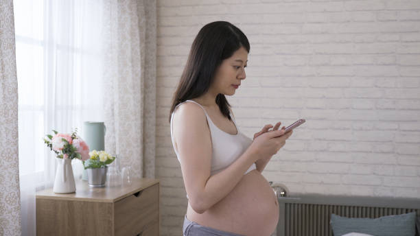 istock attractive Japanese lady in her last trimester is smiling at the camera while using smart phone texting the message at bright home interior background. 1364323578