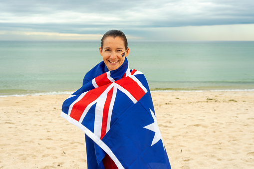Portrait of happy woman wrapped in Australian flag at beach. Concept of Australia day celebration.