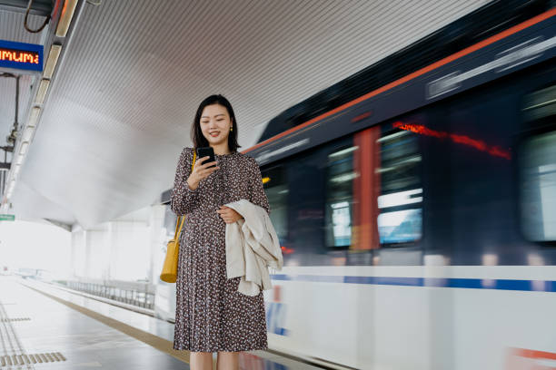 istock Asian woman using smartphone at train station 1364332773