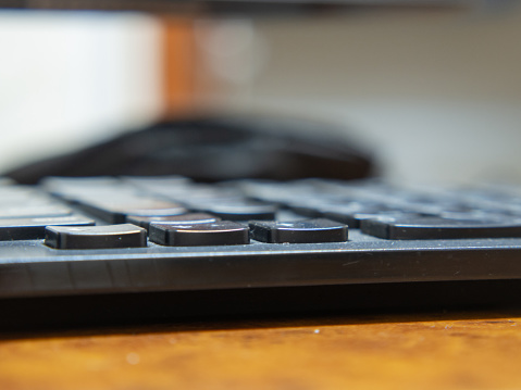 Close-up of the keys of a black computer keyboard on the office desktop, a small depth of field.  Wooden Office Desk with Working Keyboard with Traces of Use and Dust Side View with Copy Space.